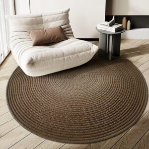 Custom woven gluefree round wool rug in brown with concentric circle pattern placed under white upholstered chair in modern living room